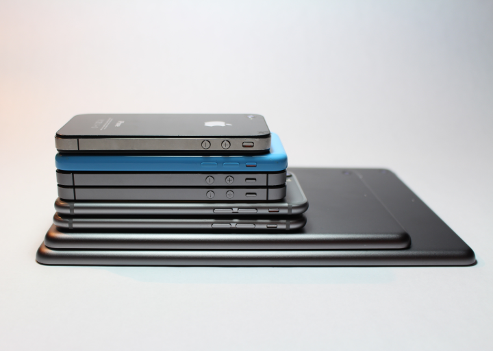 A pile of Apple products that have touchscreens. There are two iPads and 6 iPhones of different generations.